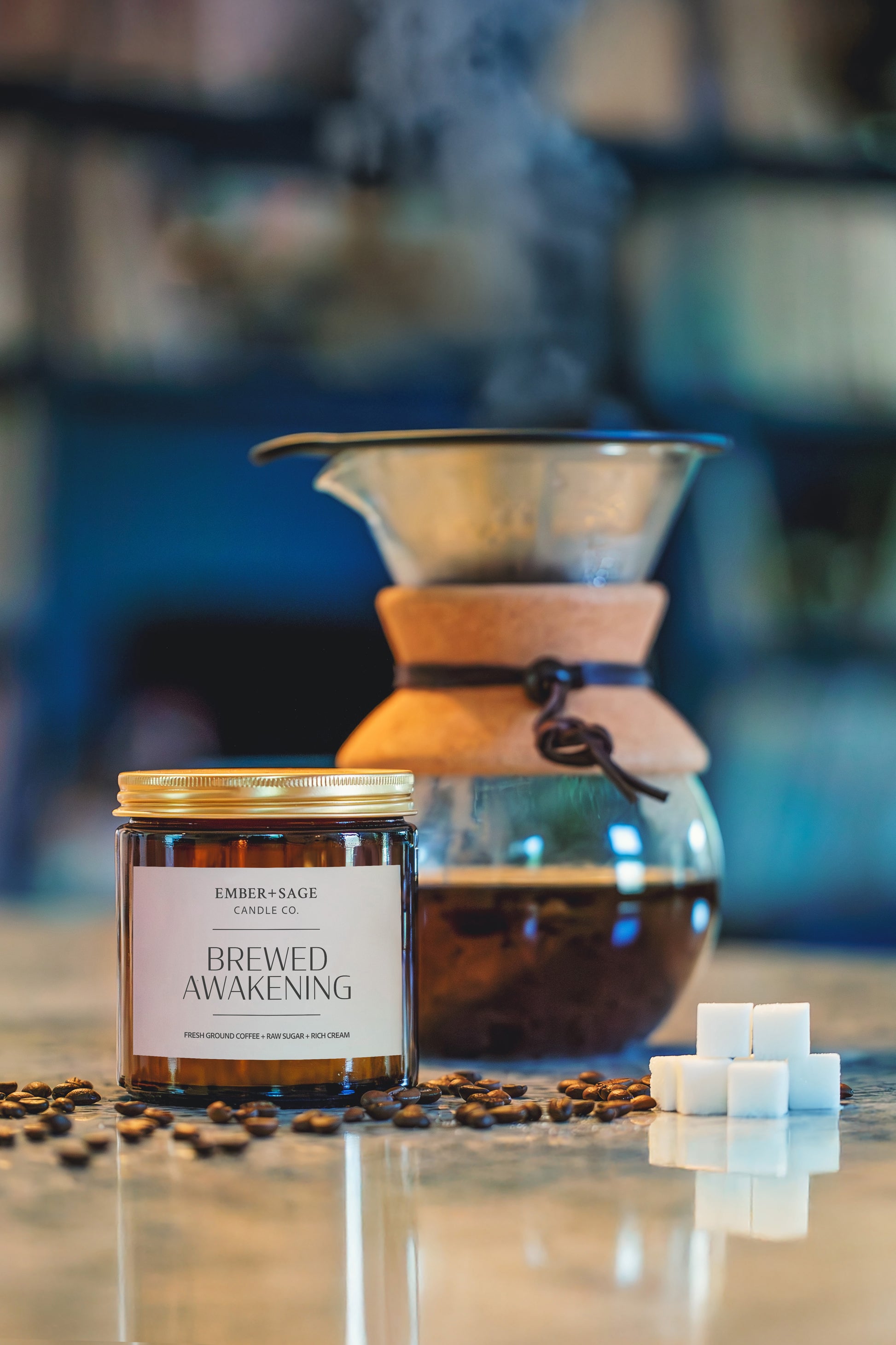Brewed Awakening hand-poured Nebraska candle in amber glass jar with coffee beans, sugar cubes, pour-over coffee maker. Fresh ground coffee, raw sugar, rich cream scent.