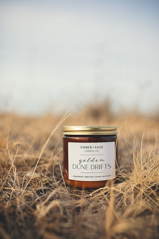 Ember + Sage "Golden Dune Dirfts" in the golden fields of the Nebraska Sandhills with notes of Sandalwood + Sweet Musk + Vetiver + Wild Violet. Made in Nebraska. Amber jar with gold lid.
